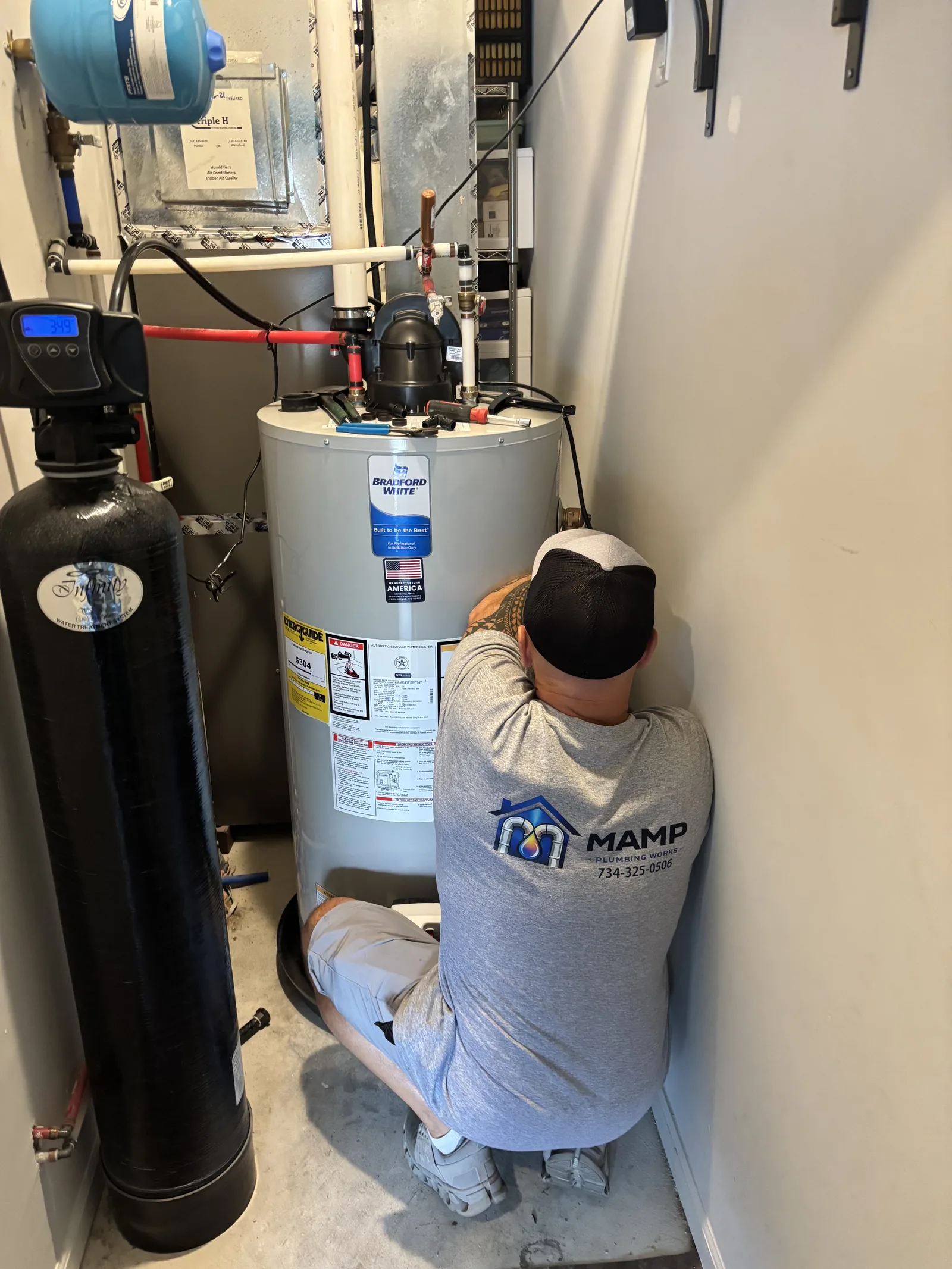 David Mamp connecting piping above a newly installed residential gas water heater next to a water softener tank